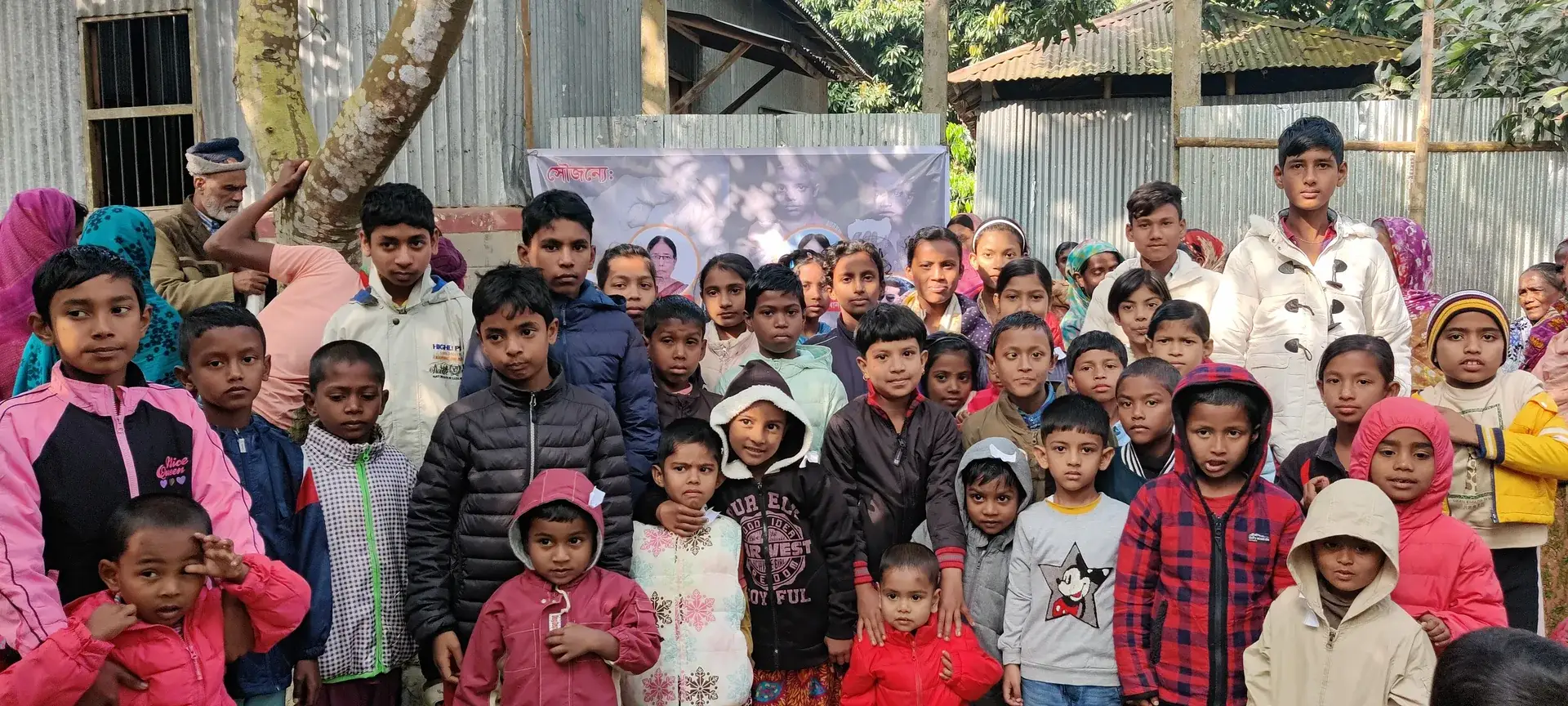 A large group of village children in warm clothes gathered outdoors in Chatlarpar during a winter clothes distribution.